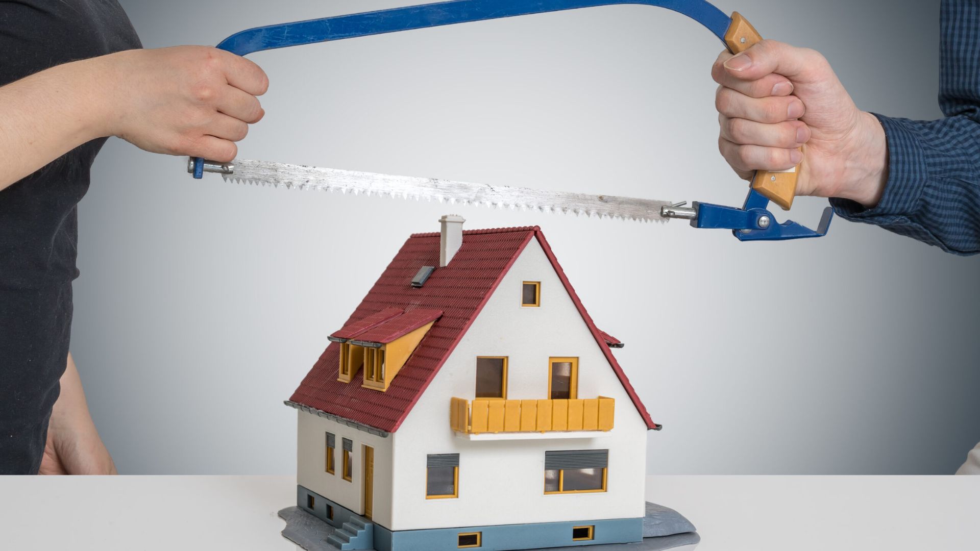 A man uses a saw on a model house, demonstrating a woodworking technique or project.