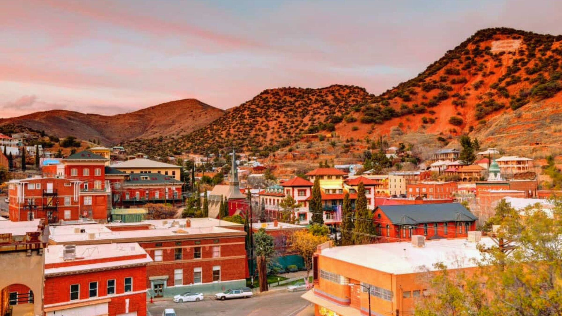 A scenic town featuring red buildings with majestic mountains rising in the background.