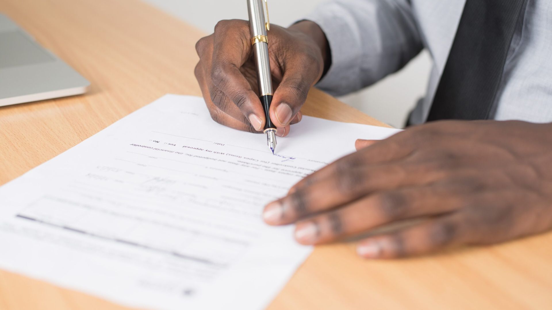 A man dressed in a suit is engaged in signing an important document, demonstrating professionalism.
