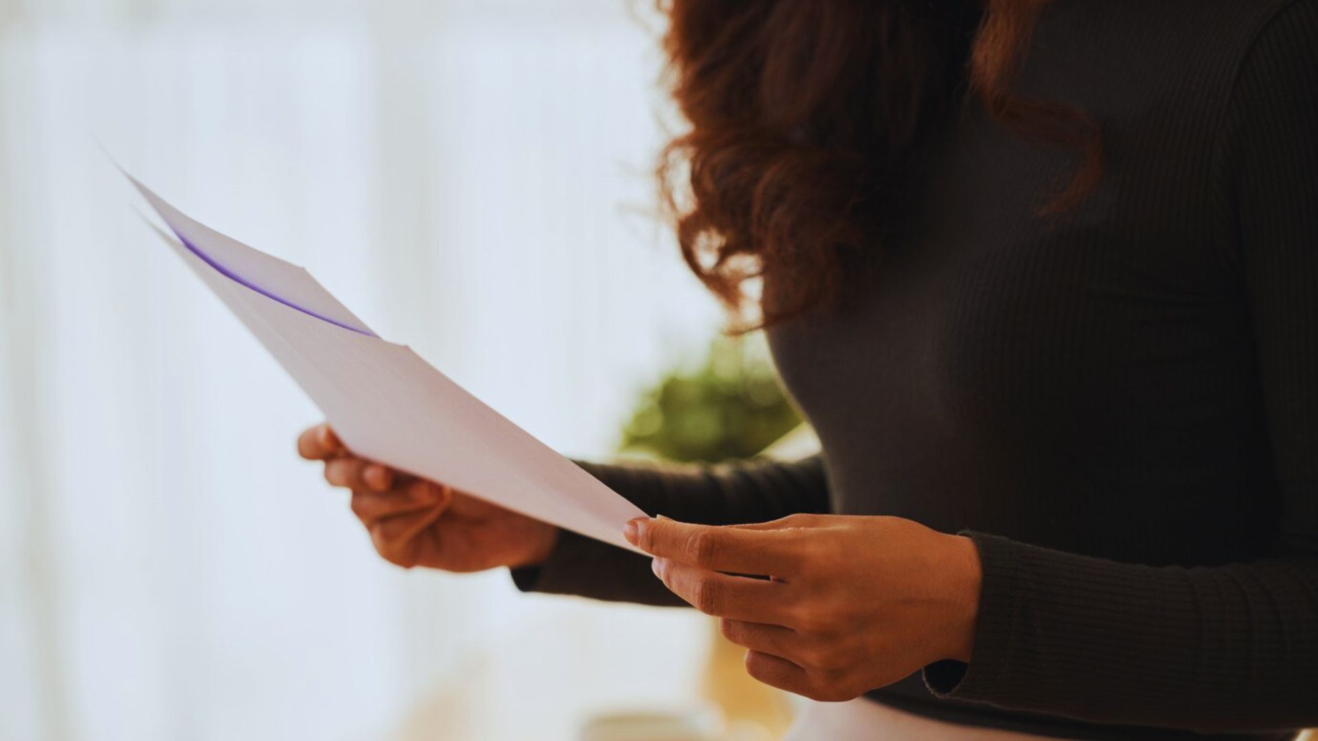A woman is holding a piece of paper and intently examining its contents.