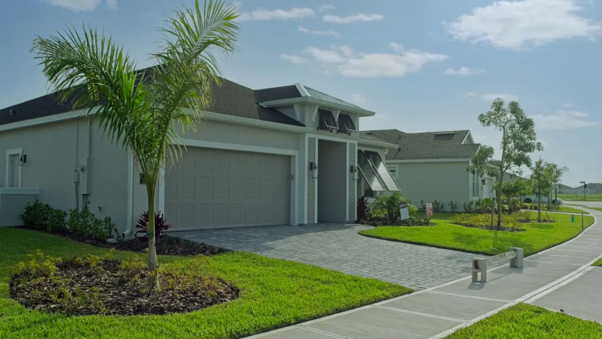 A house with a driveway surrounded by lush palm trees under a clear blue sky.