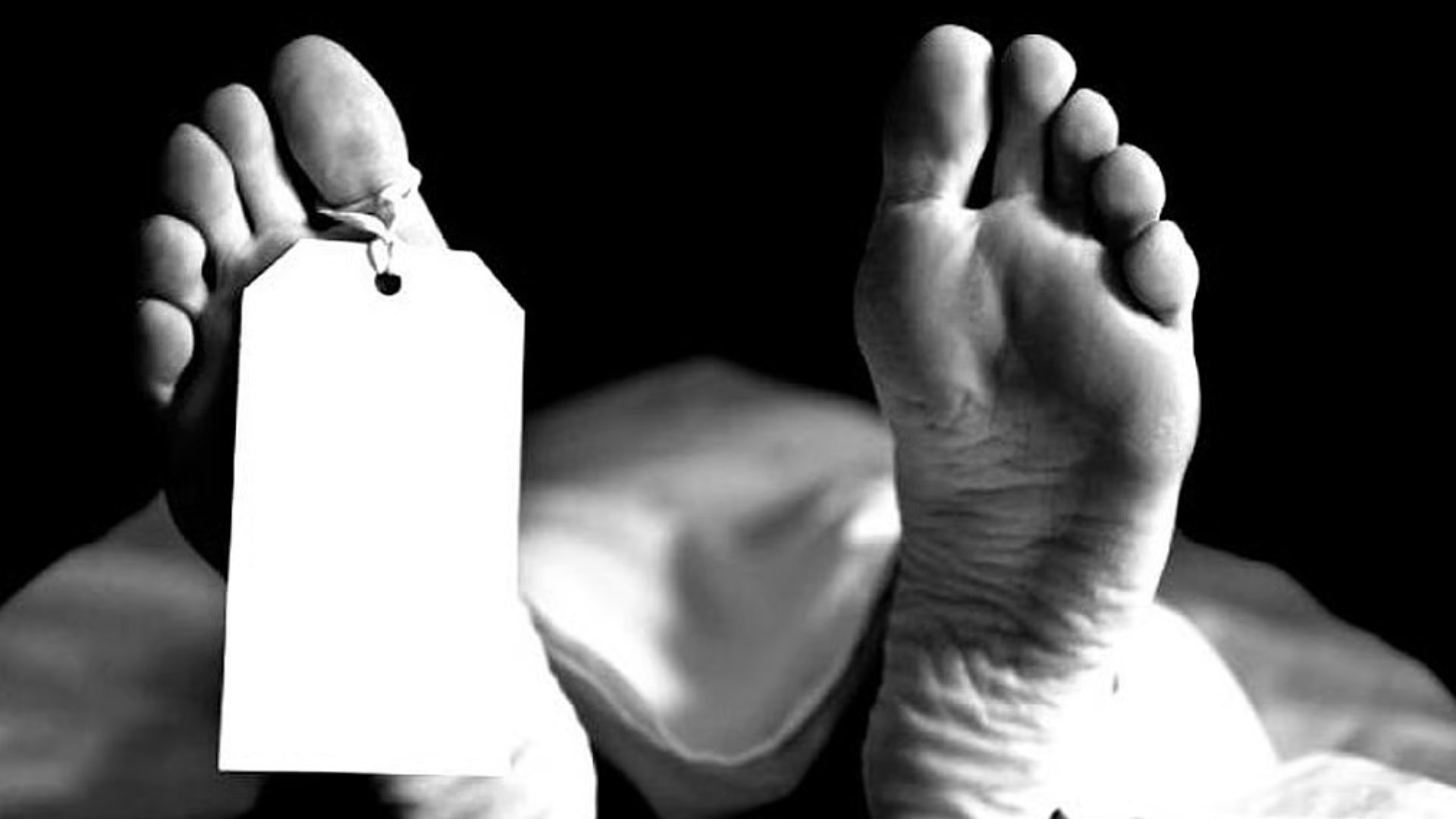 A person's feet resting on a bed, with a white tag visible near the foot of the bed.