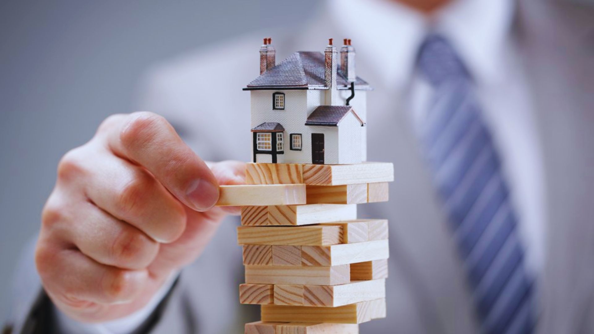 A man holds a wooden house atop a stack of colorful blocks, symbolizing creativity and construction.