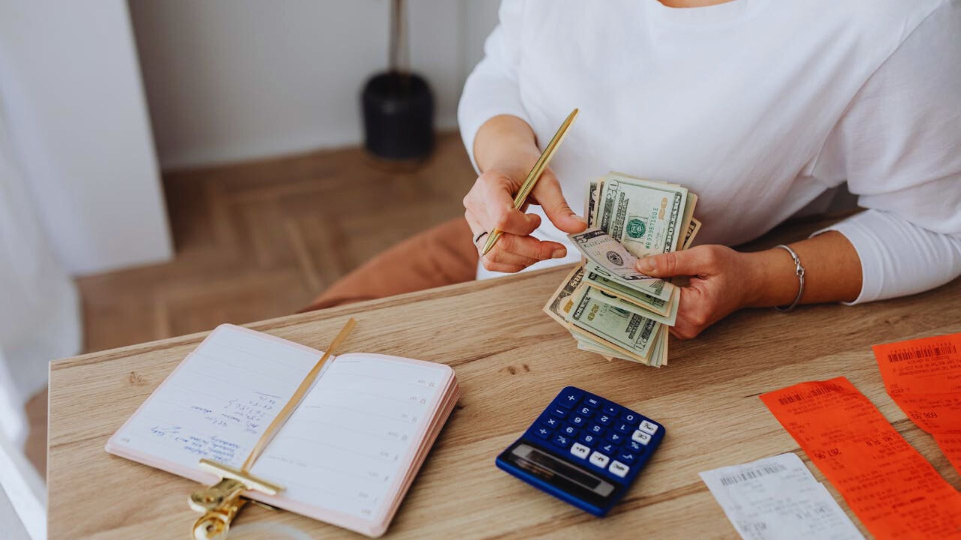 A woman counts money on a table, using a calculator and pen for calculations.