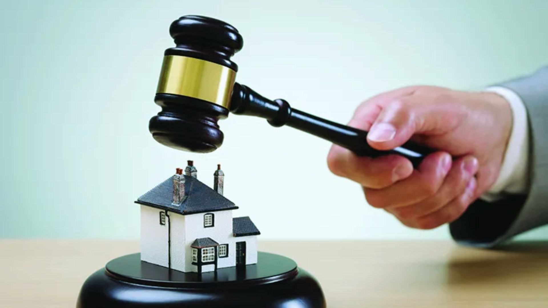 A judge's gavel is poised above a small model house, symbolizing legal authority over housing matters.