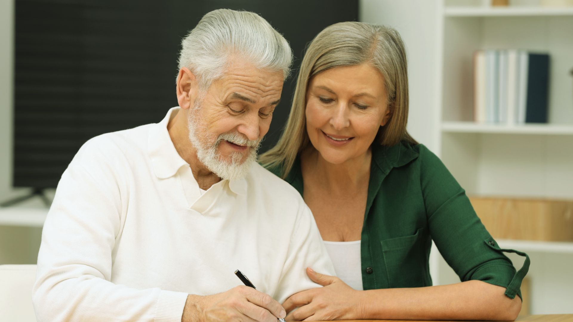 A senior couple collaboratively signing a document, demonstrating teamwork and mutual agreement.