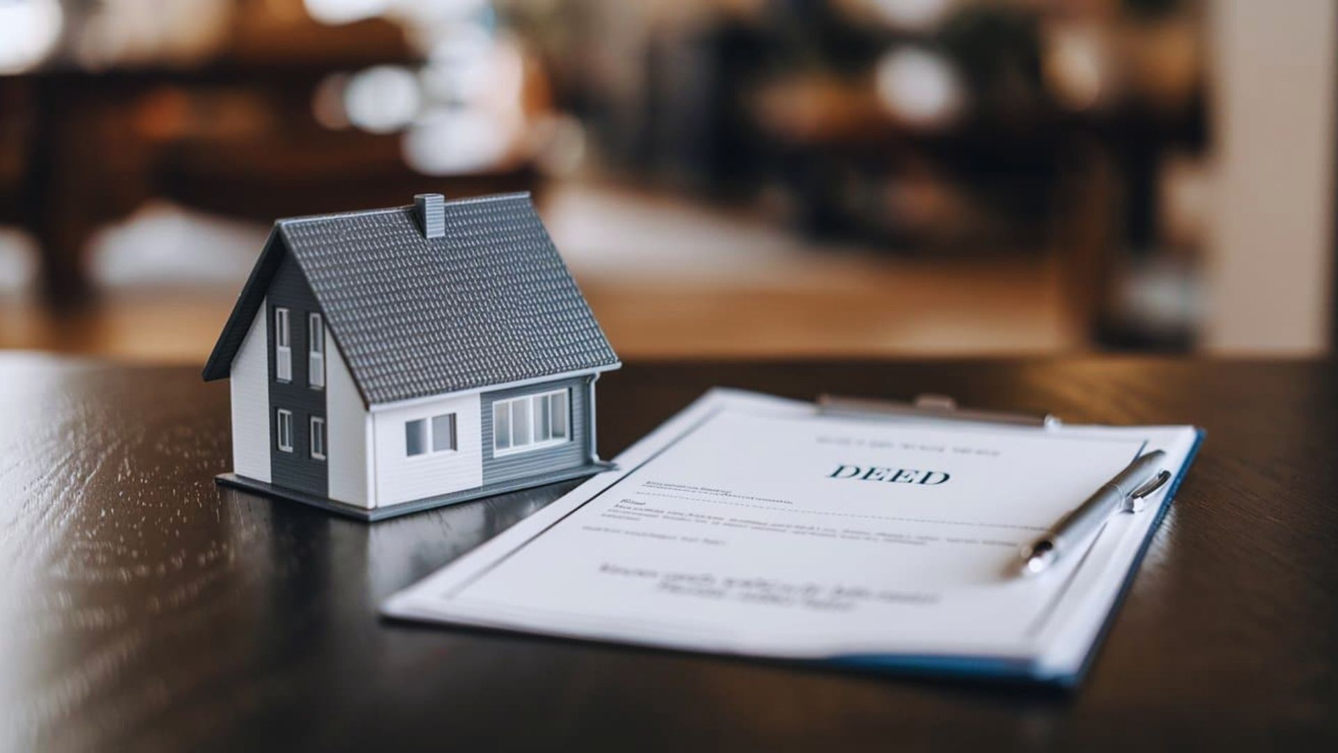 A house model and a pen are placed on a wooden table, showcasing a miniature architectural design.