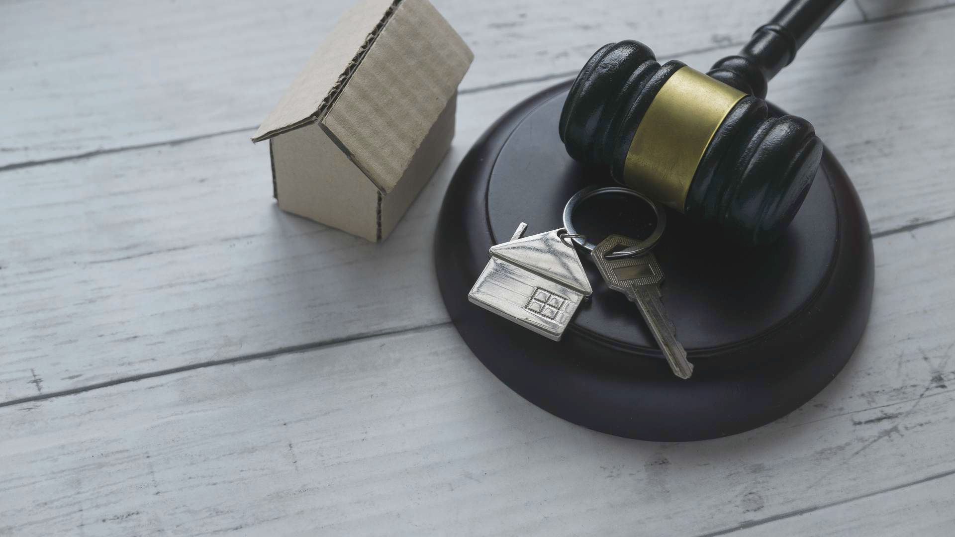 A gavel, a house key, and a model house arranged on a wooden table, symbolizing real estate and legal matters.