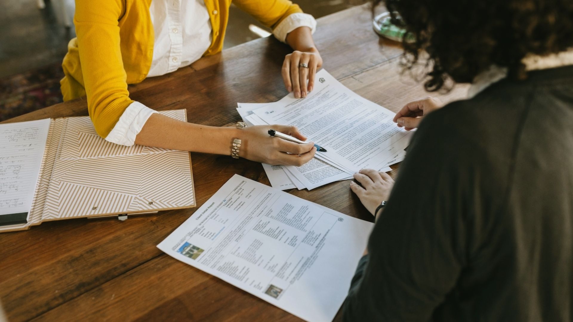 Two women at a table, engaged in discussion with papers and a pen in front of them.