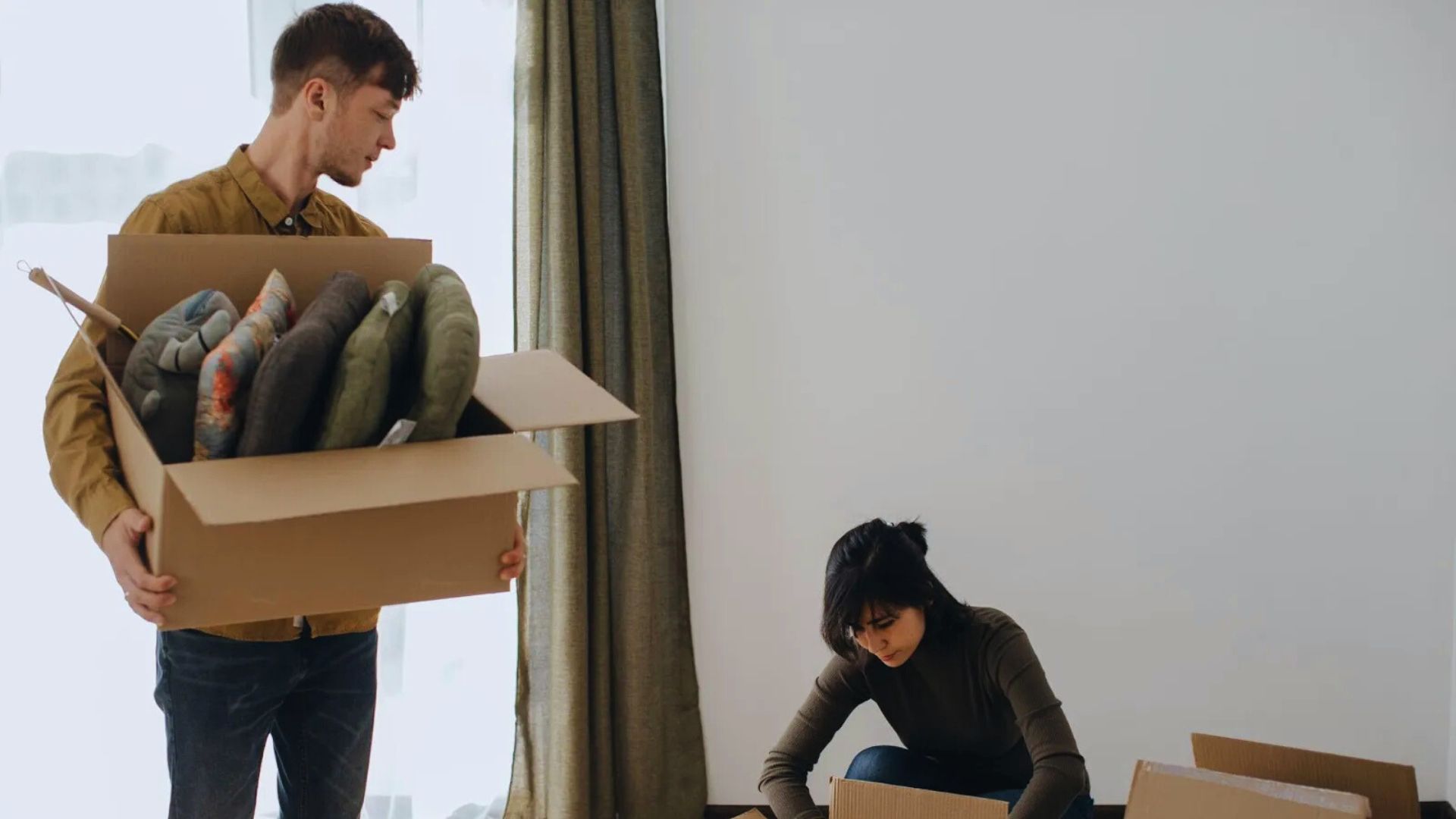 A man and woman are carrying boxes into a room, preparing for a move or organizing the space.