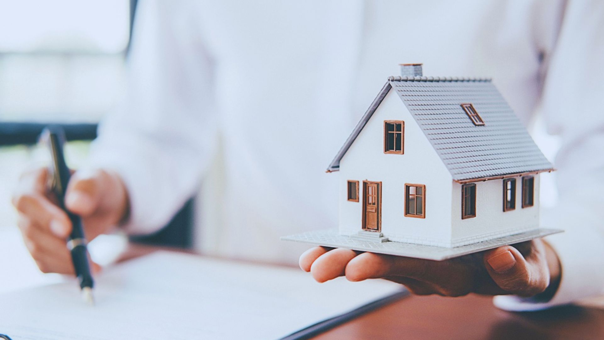A real estate agent holds a small house model in his hands, showcasing it to potential clients.