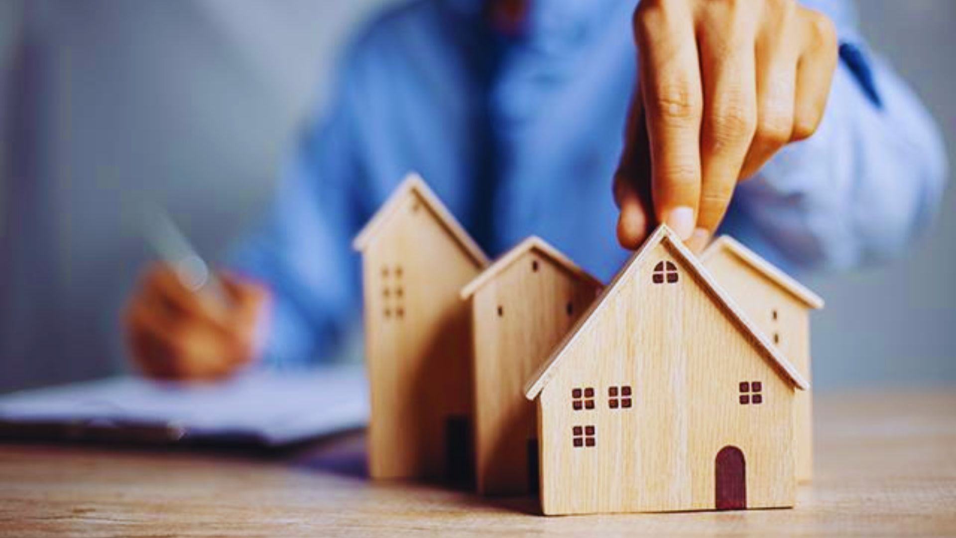A person holding a small wooden model of a house, showcasing intricate details and craftsmanship.