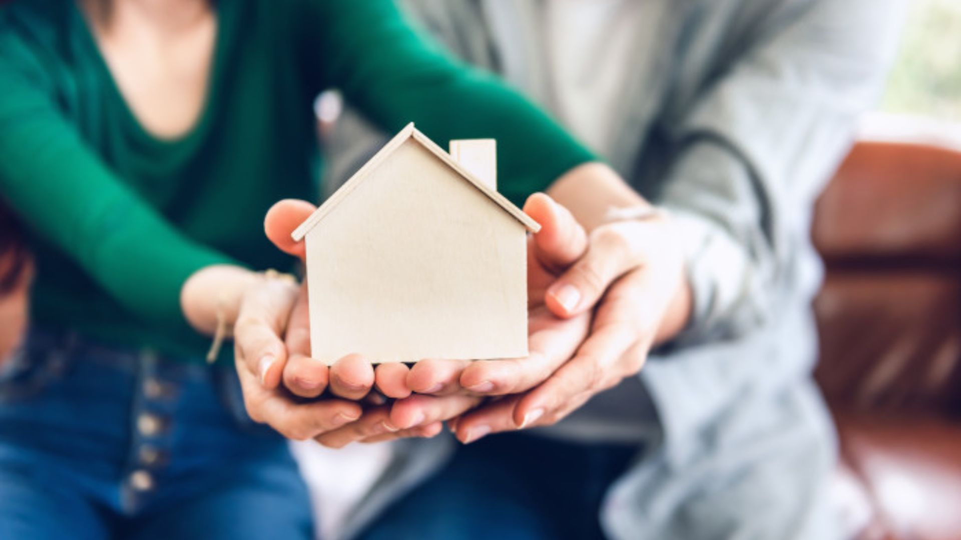 A couple smiles while holding a small house model together in their hands, symbolizing their dream of homeownership.