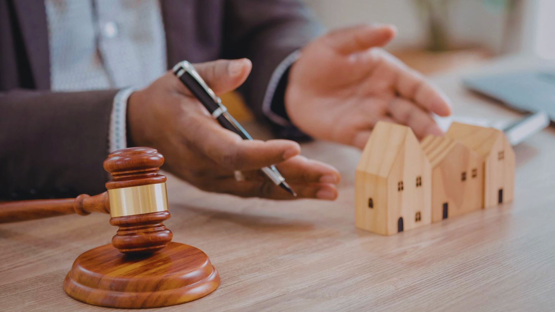 A man in a suit holds a wooden gavel and a model house, symbolizing authority in real estate or legal matters.