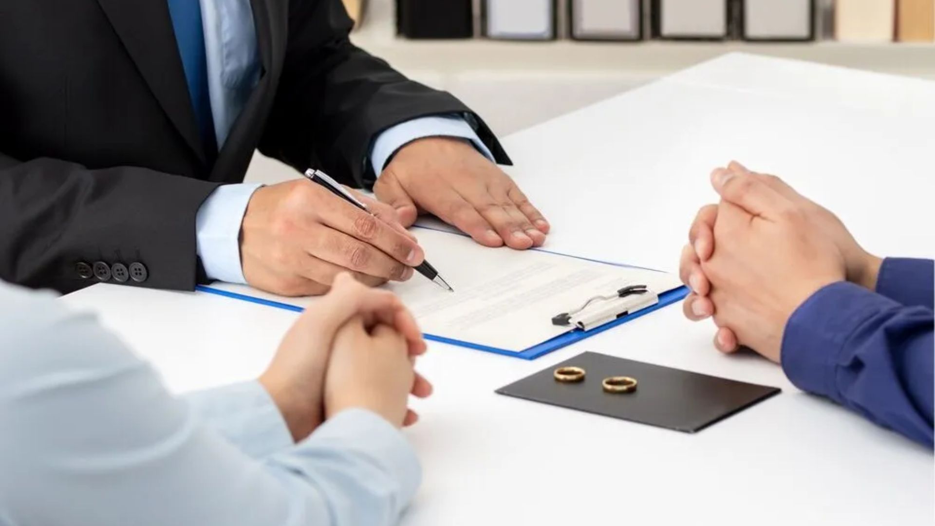 A man signs a contract while two other individuals observe attentively at the table.