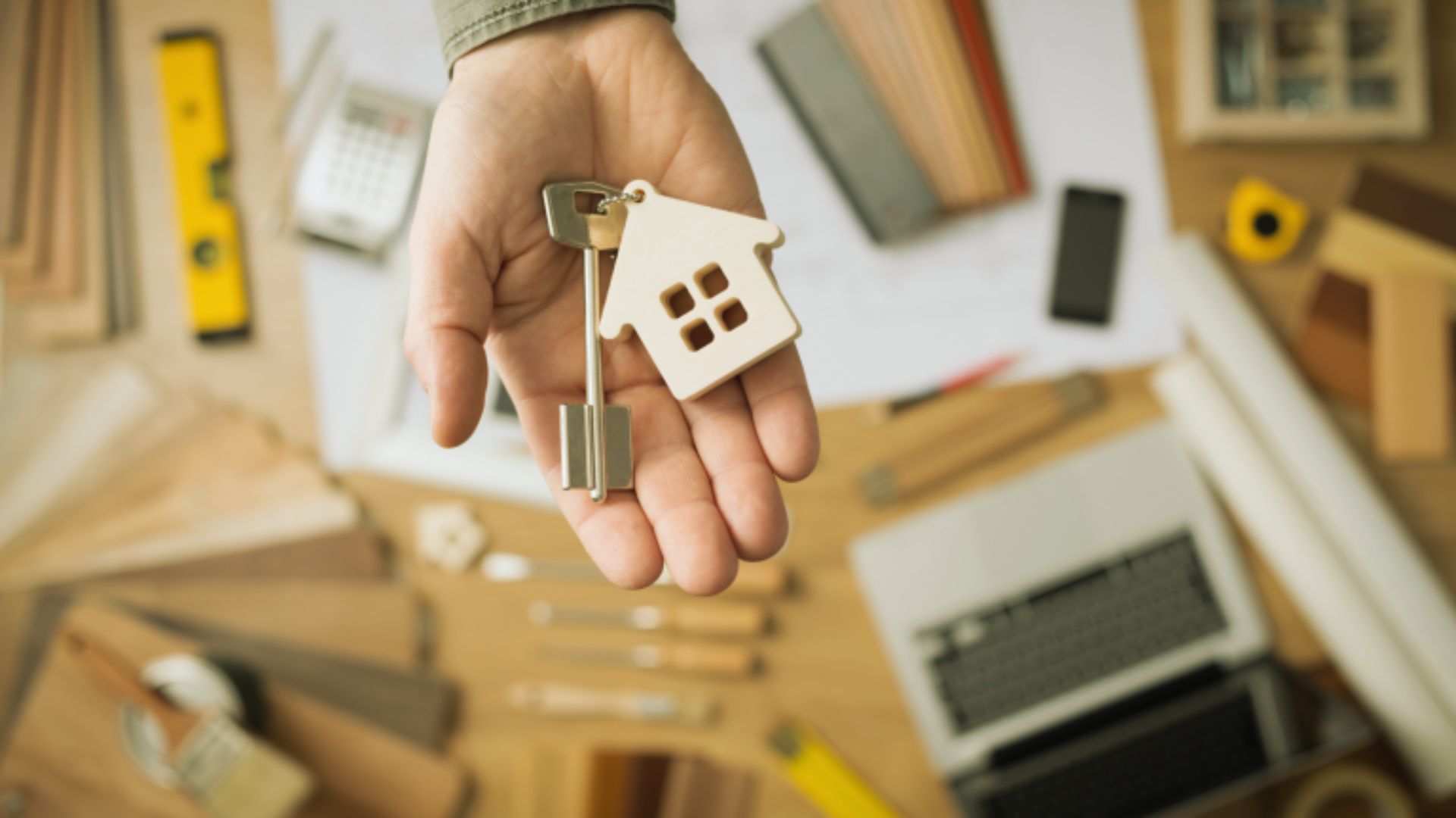 A person holds a house key in one hand and a small model house in the other, symbolizing home ownership.