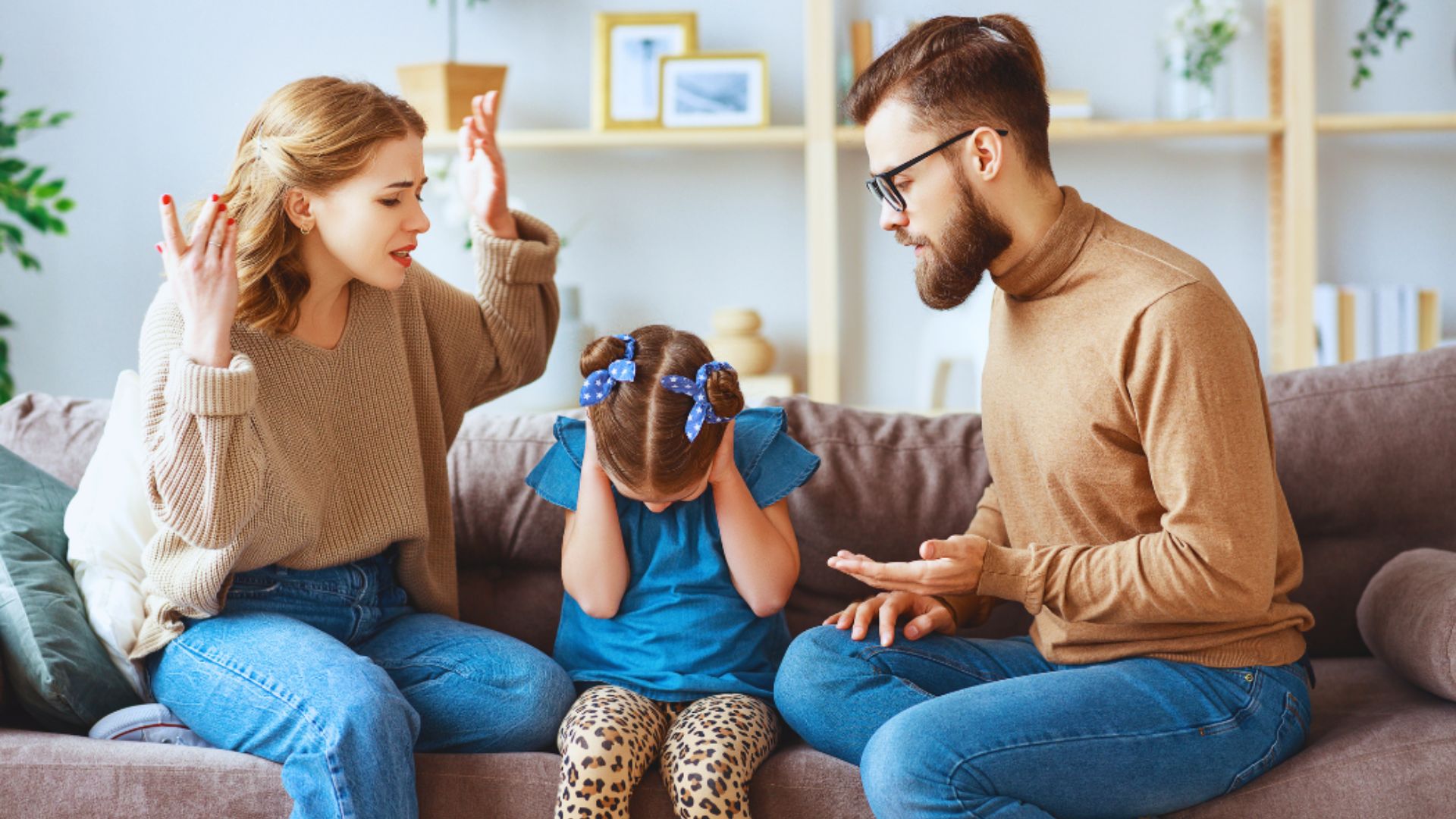A man and woman sit on a couch with a little girl, all smiling and enjoying a cozy family moment together.