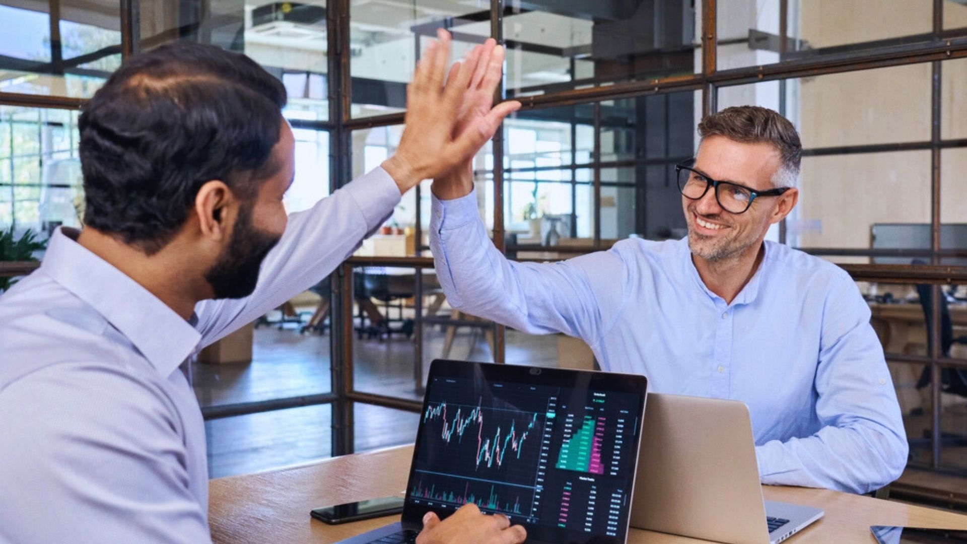 Two men in business suits high five each other, celebrating a successful collaboration or achievement.