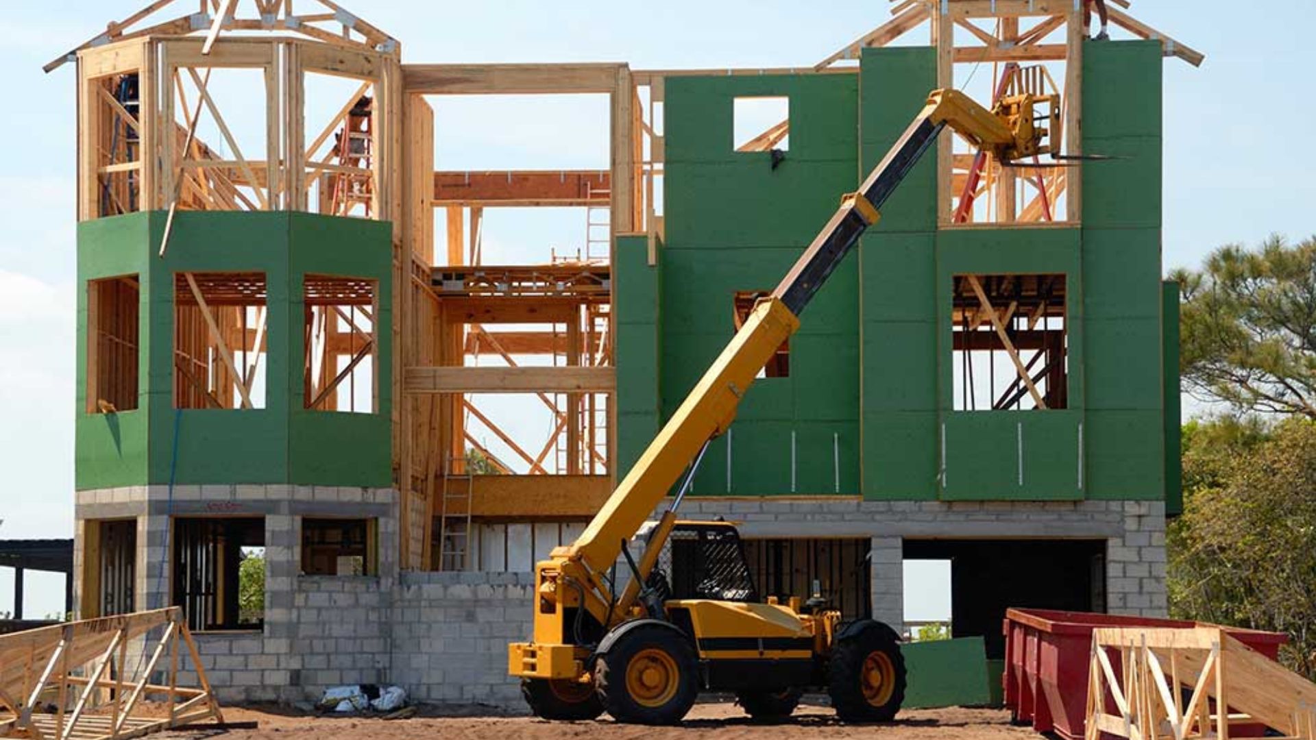 A construction worker is actively building a house, wearing a hard hat and using tools on the construction site.