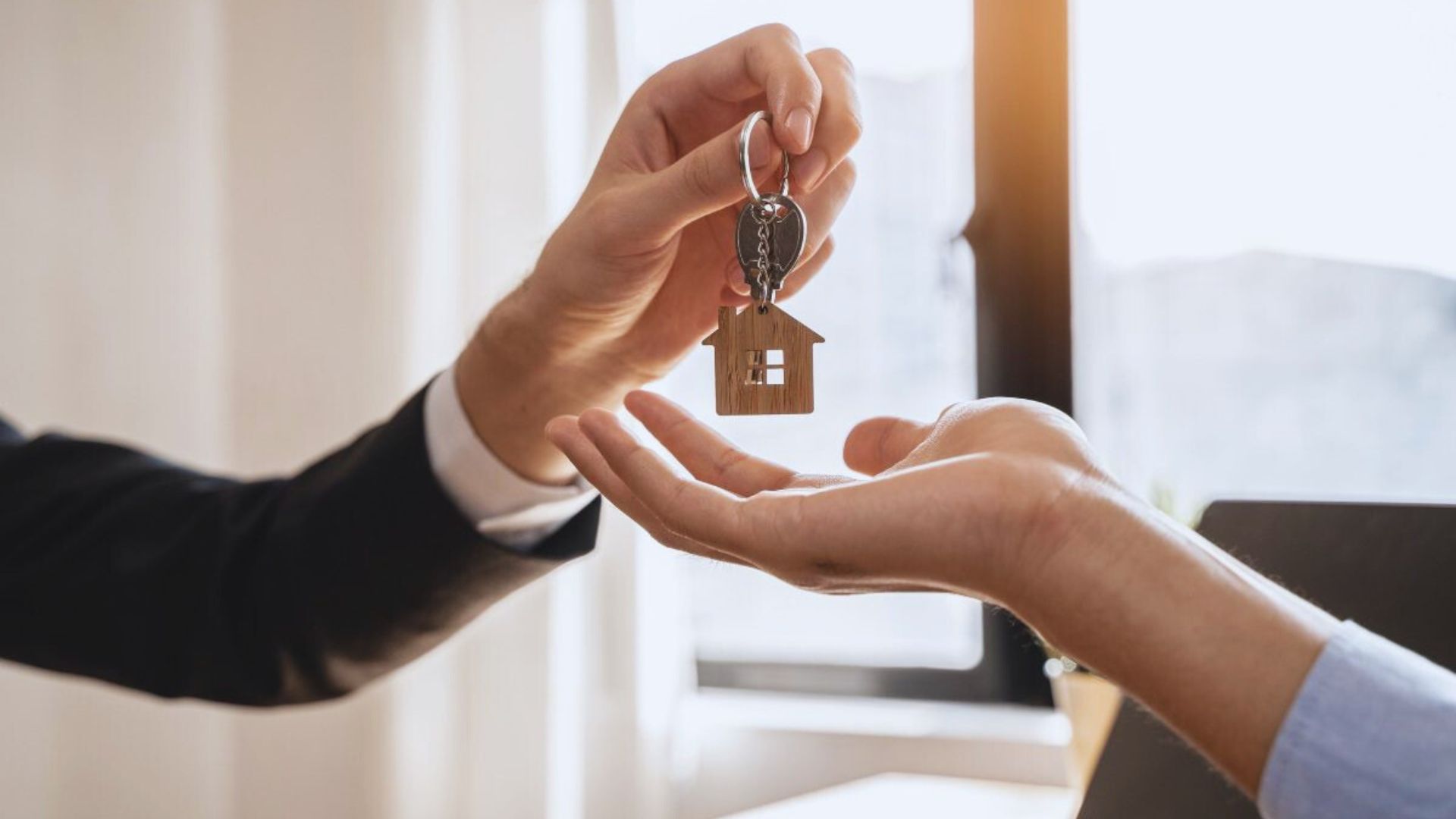 A person hands a house key to another, symbolizing the transfer of home ownership or rental agreement.
