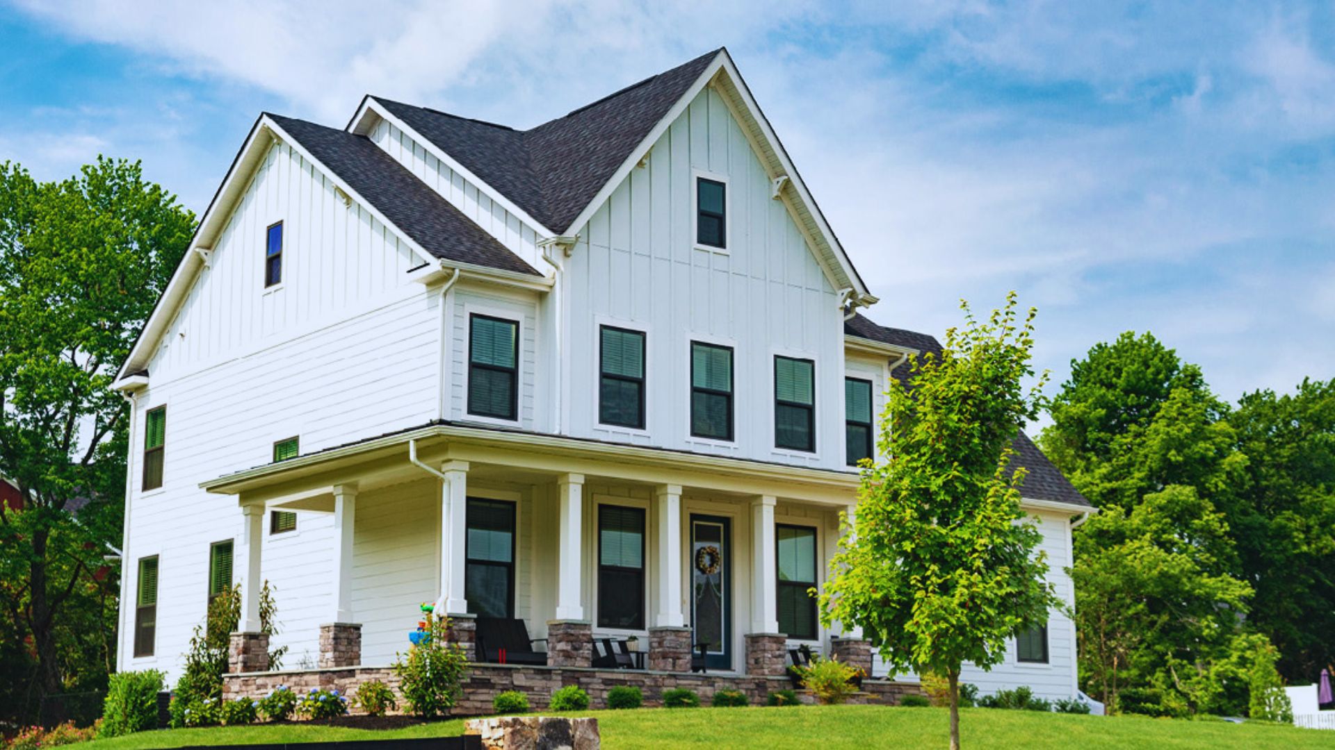 A white house featuring a spacious front porch, surrounded by greenery.
