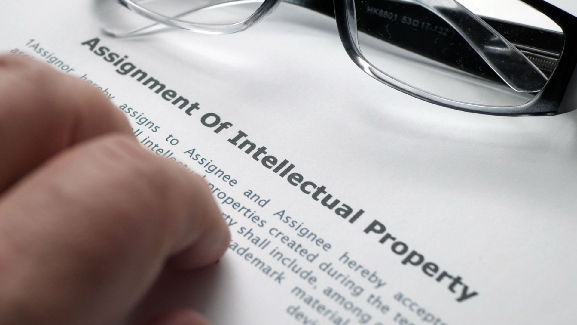 Document titled "Assignment of Intellectual Property" with legal text and signatures on a wooden desk.