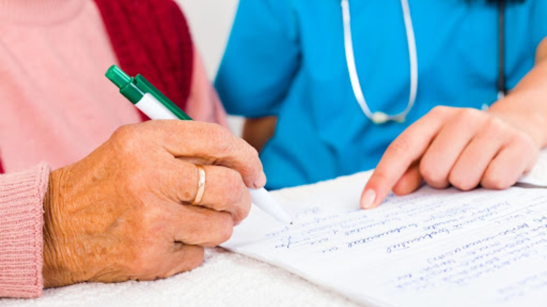 A nurse assists an elderly woman by signing a document together in a healthcare setting.