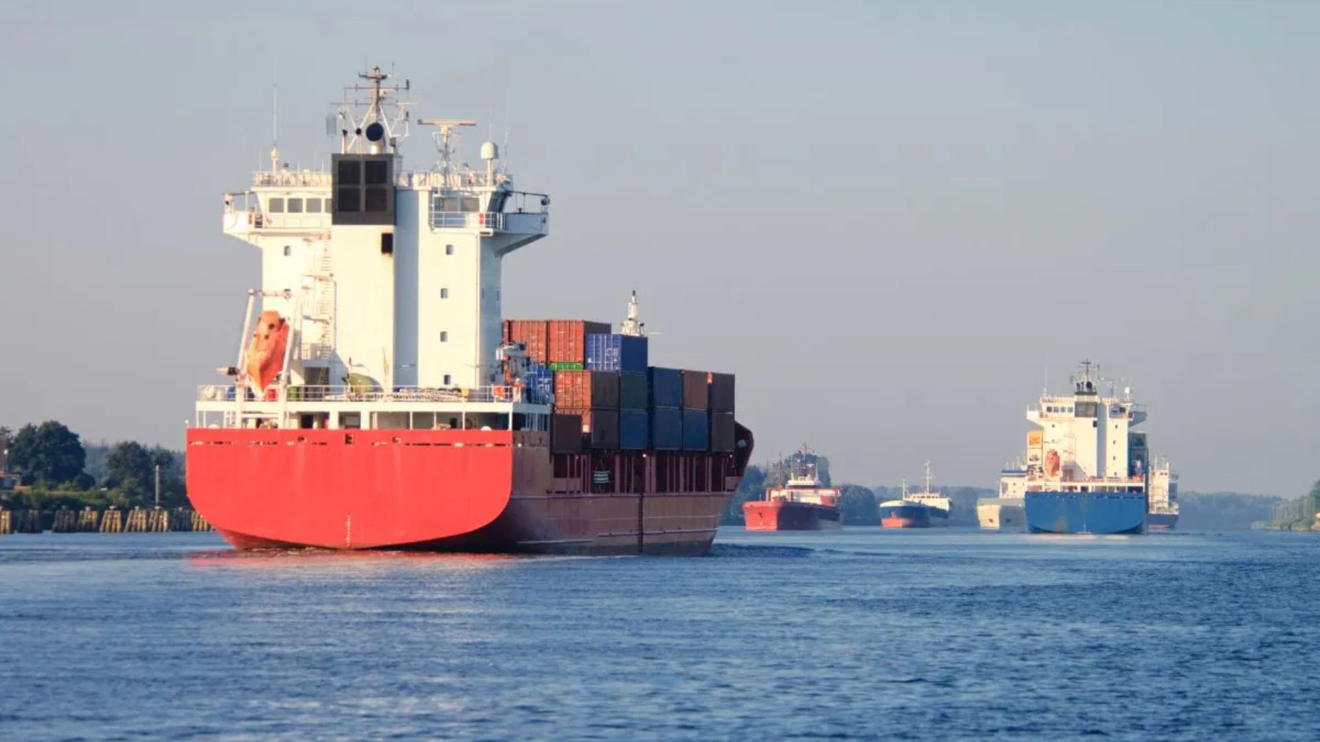 A large container ship navigates down a river, surrounded by water and greenery along the banks.