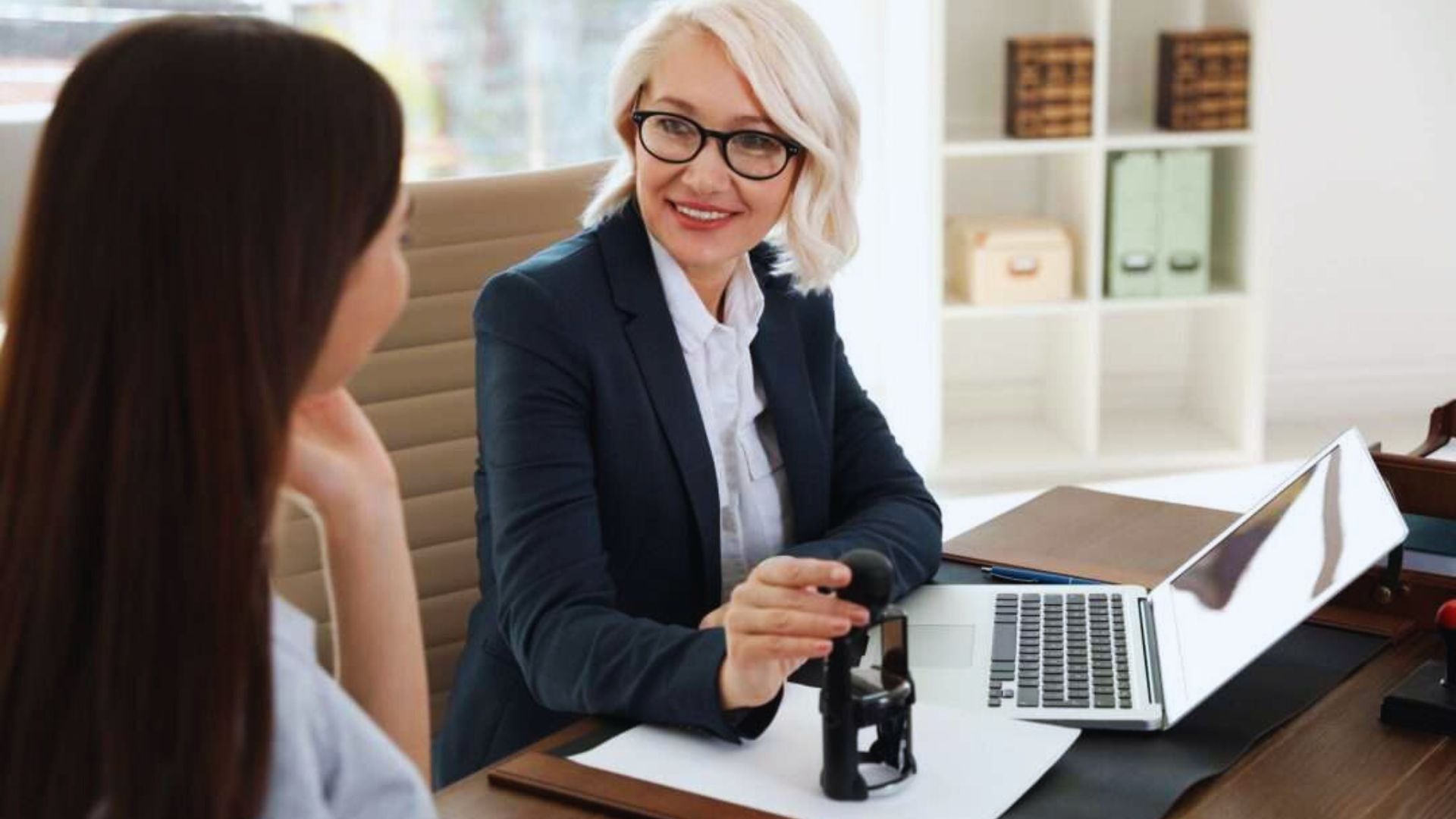 A woman in a business suit engages in conversation with another woman.