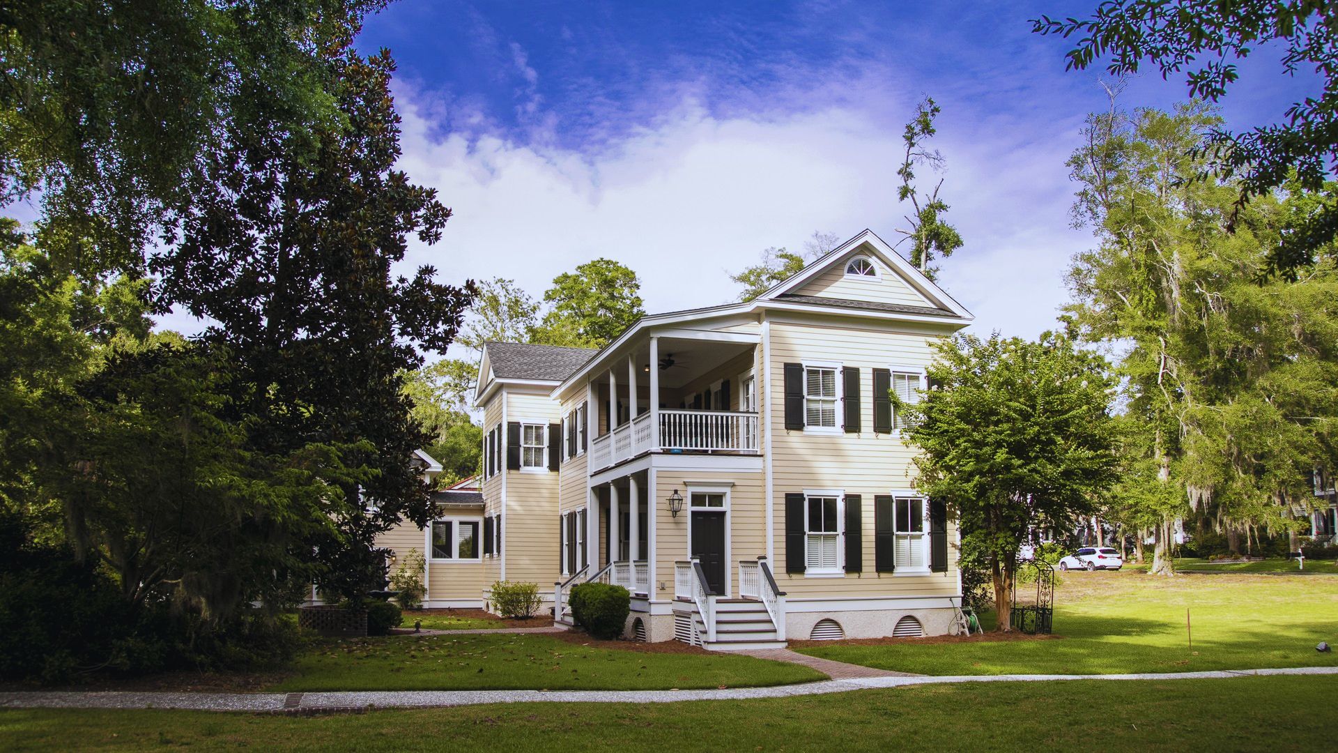 A large white house with a porch surrounded by a tree, showcasing a classic suburban architectural style.