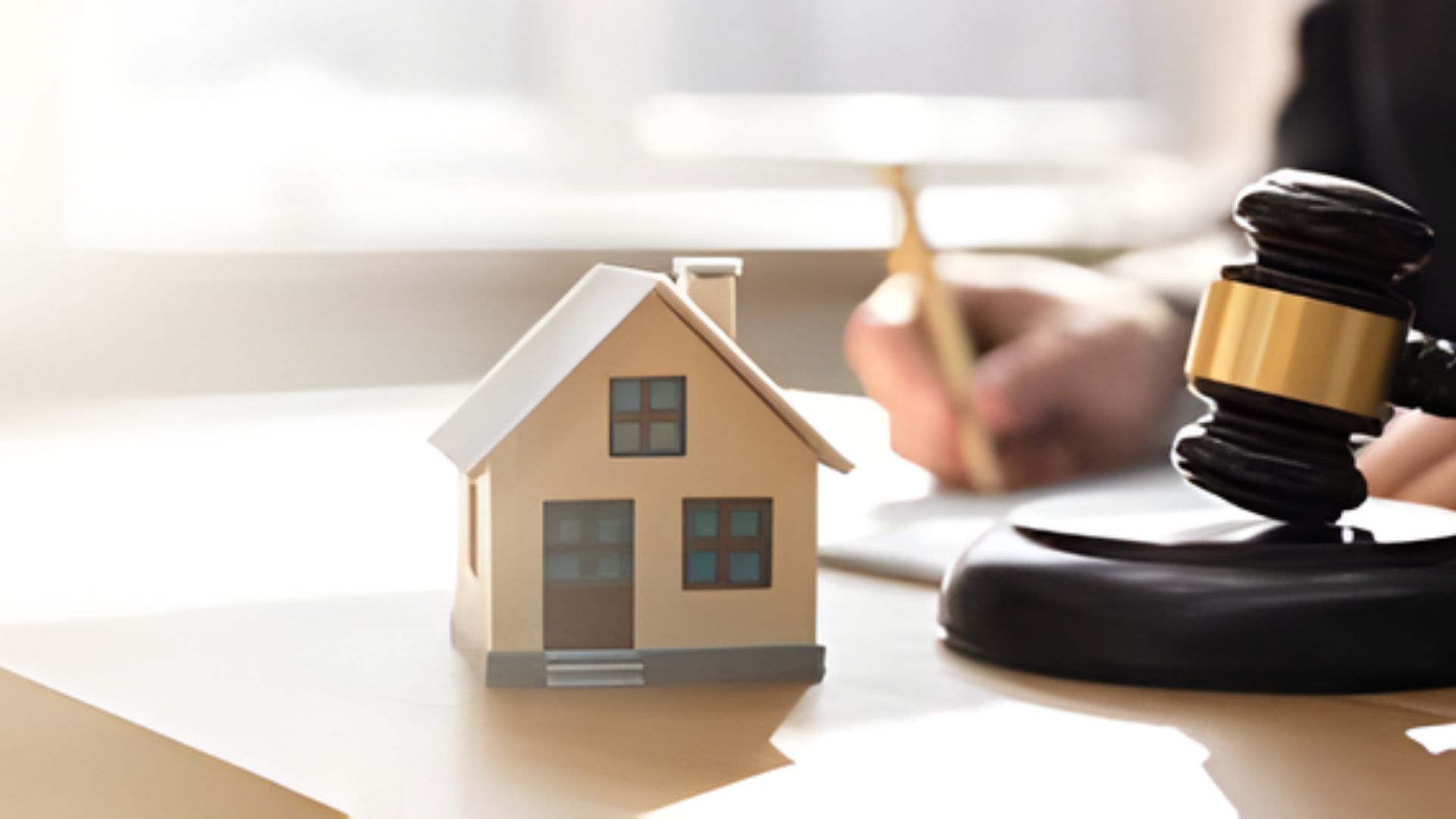 A judge's gavel rests on a desk beside a small model of a house, symbolizing legal matters related to real estate.
