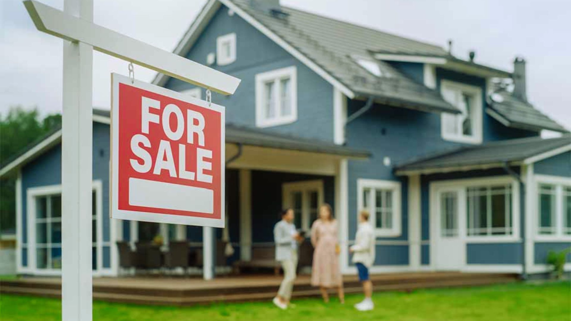 A for sale sign stands in front of a house, indicating the property is available for purchase.