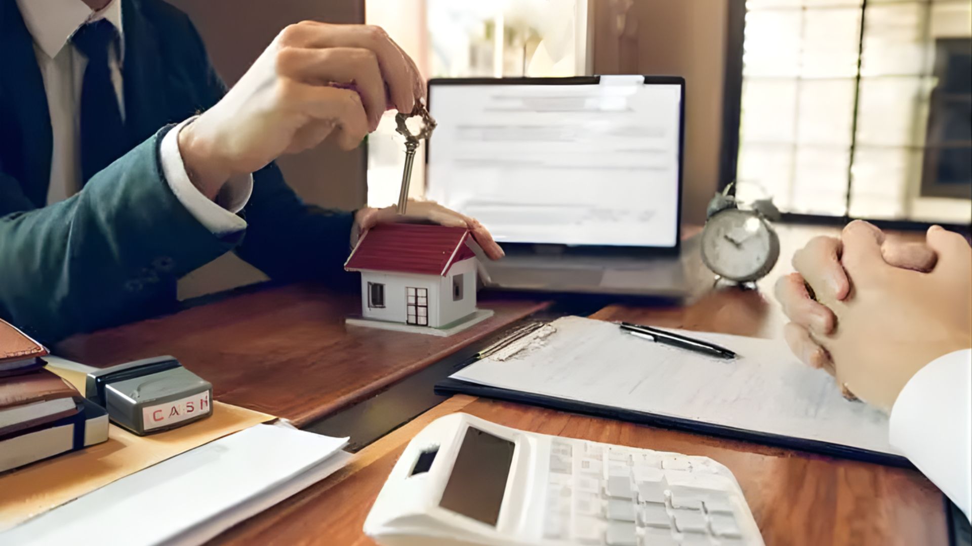 A man holds a house key, with a calculator and laptop on a table, symbolizing home ownership and financial planning.