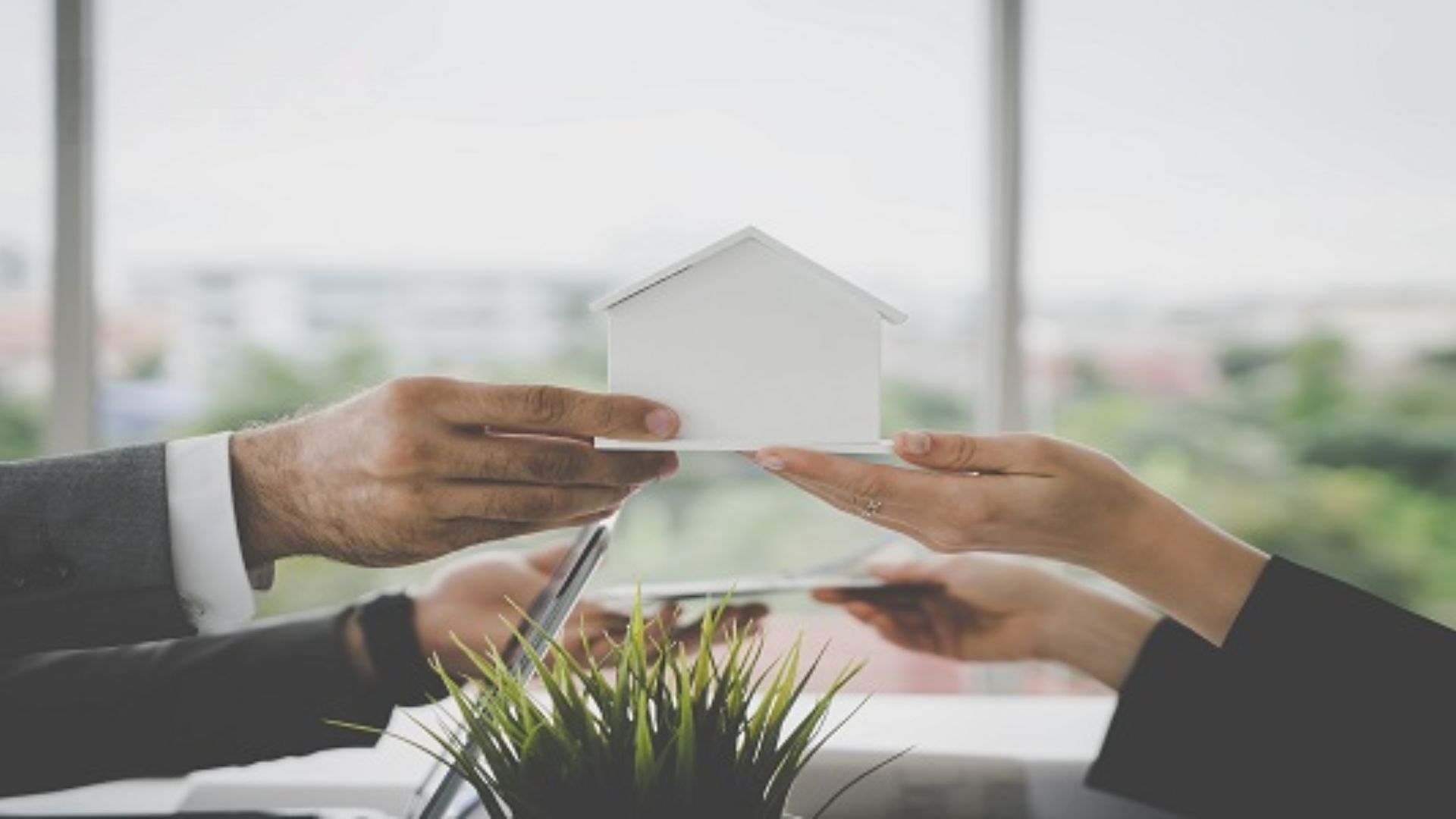 Business professionals presenting a house model in front of a table during a meeting.