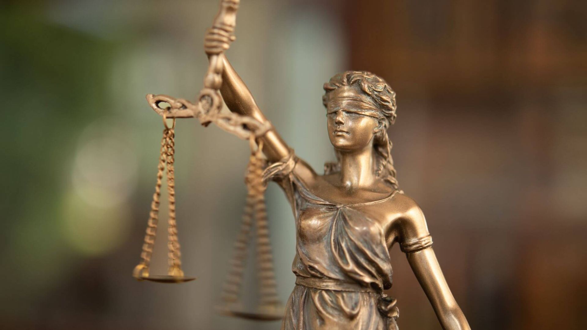 Close-up of a bronze Lady Justice statue, blindfolded, holding scales and a sword. Represents fairness and law, with a solemn, impartial expression.