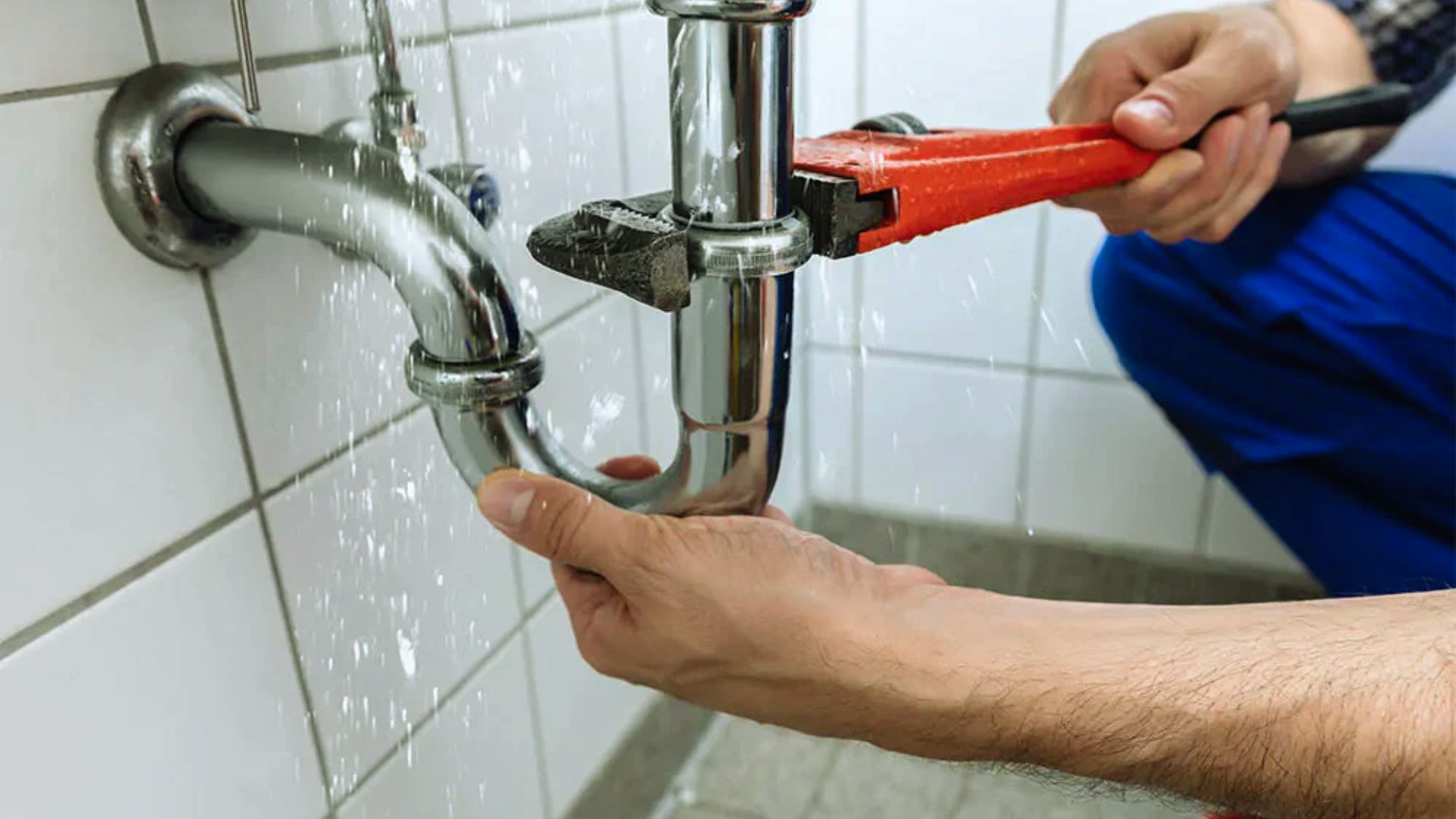 A man uses a wrench to repair a pipe, focusing intently on the task at hand.