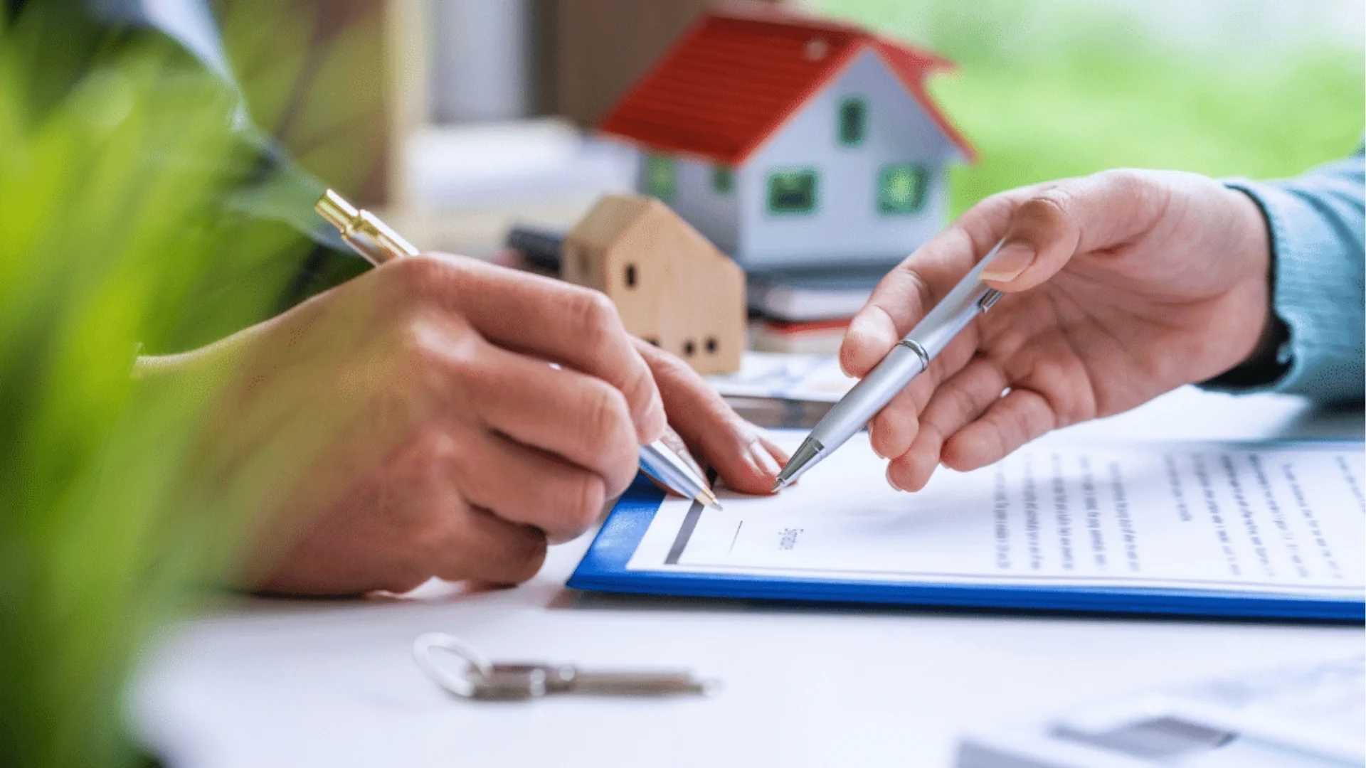 A real estate agent and a client signing a contract at a desk, with documents and a pen visible.