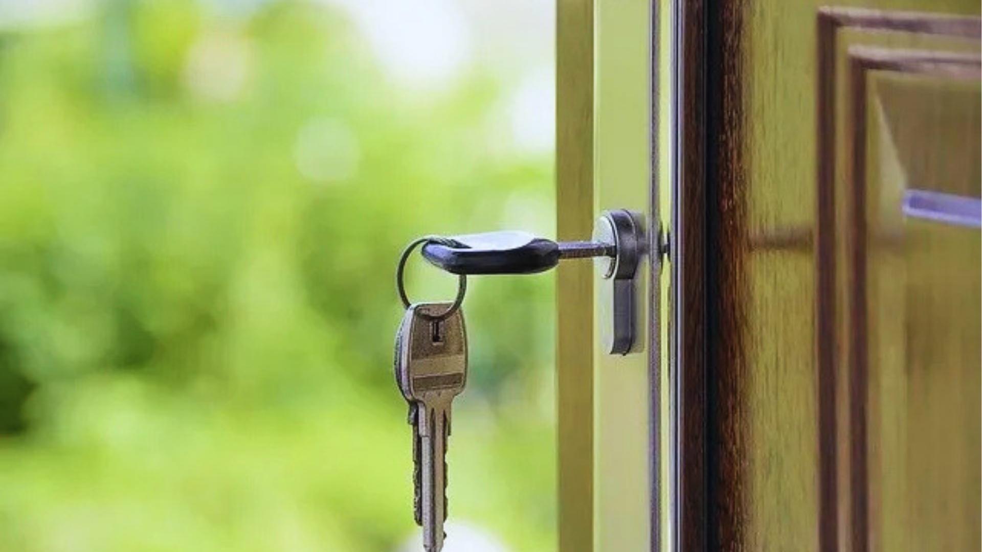 Close-up of silver house keys hanging from key in wooden door lock with blurred green yard, symbolizing property access and ownership.