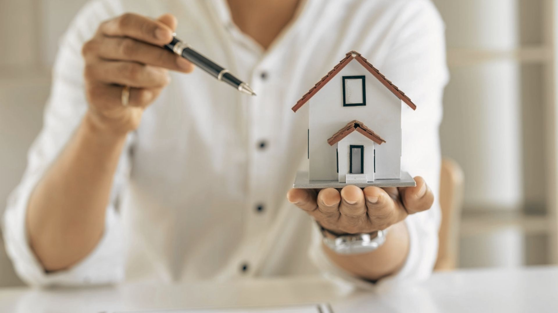 a man holds a small house model, symbolizing property often left outside a trust.