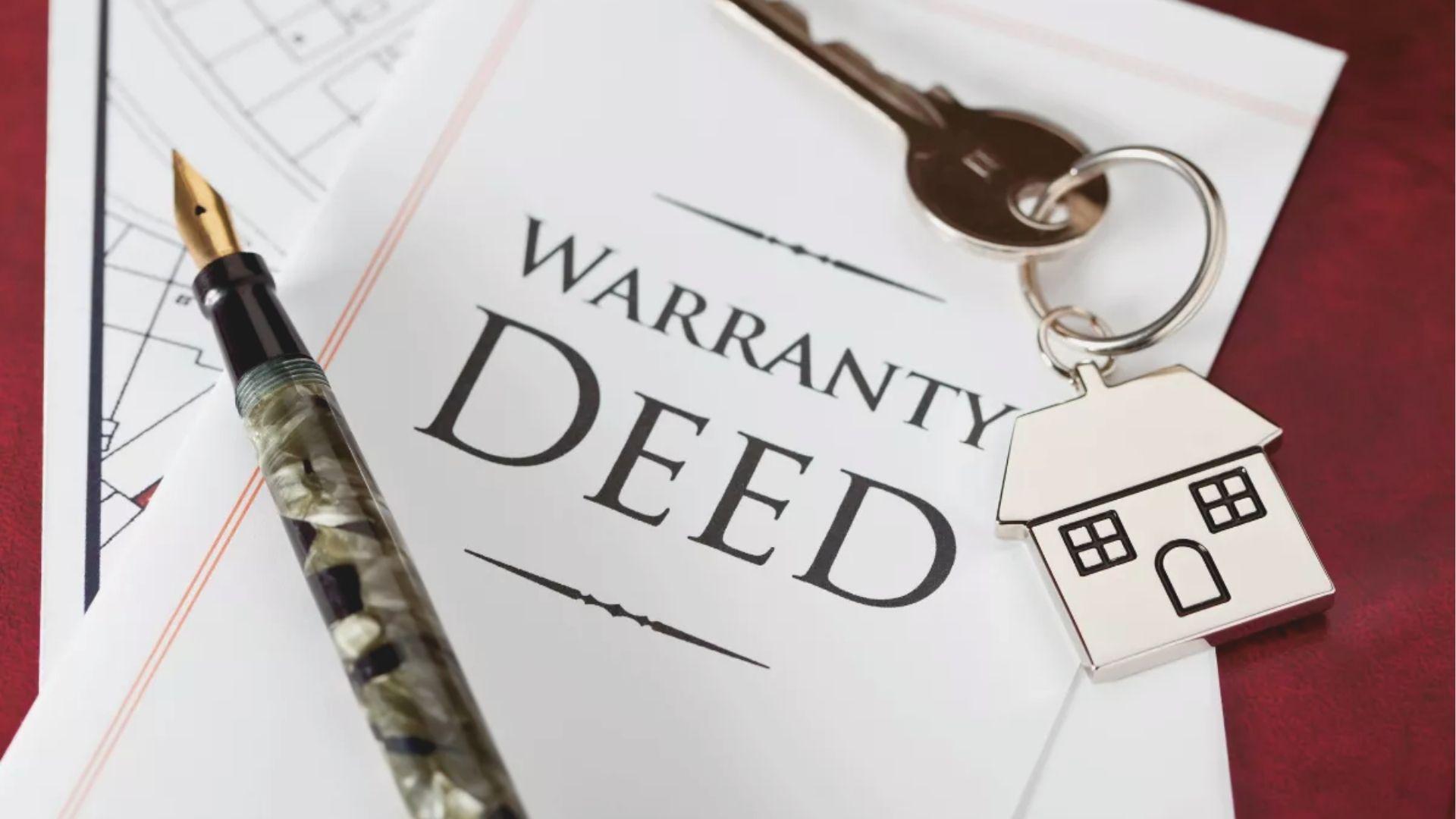 Close-up of a printed “WARRANTY DEED” document with a fountain pen and house-shaped keychain resting on top.