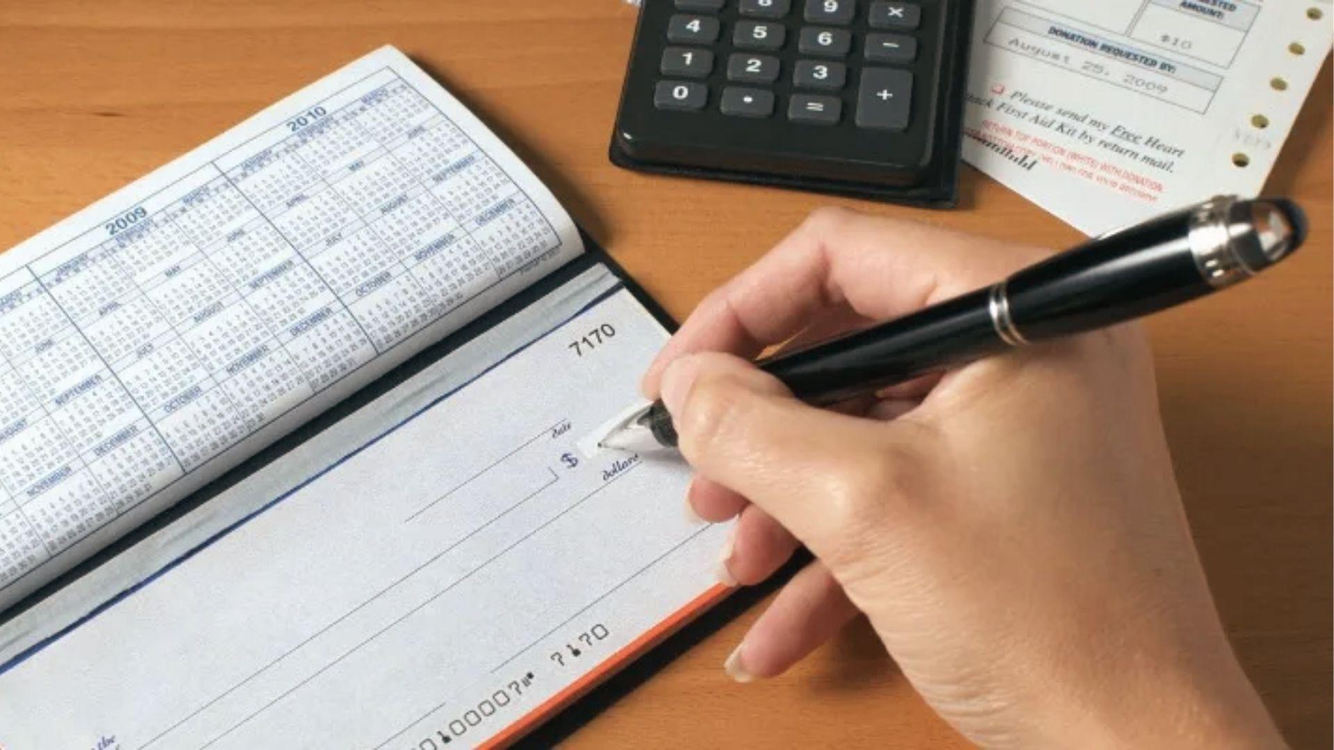 Hand writes check with calculator nearby to illustrate estate account vs trust account fund transfers