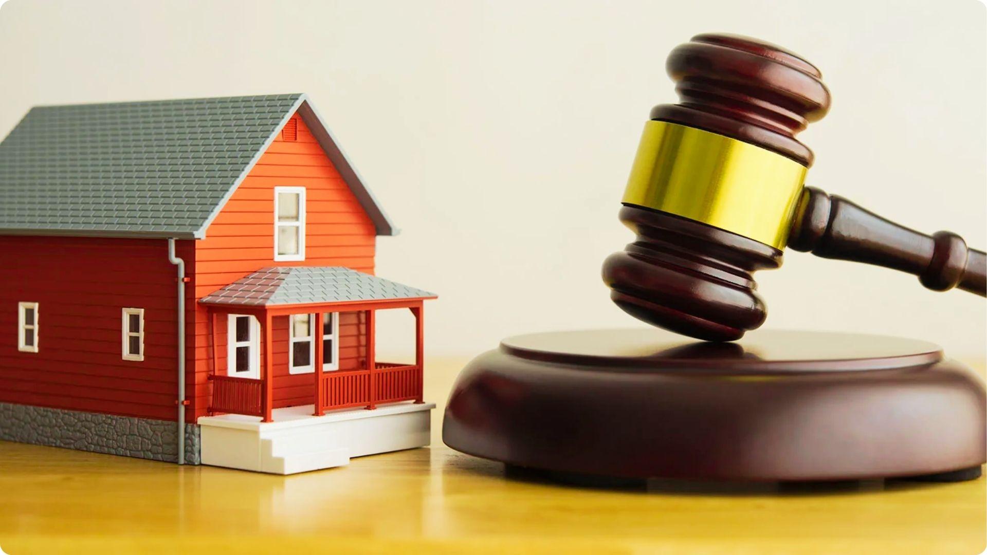 Small red model house next to a judge’s gavel on a wooden table.