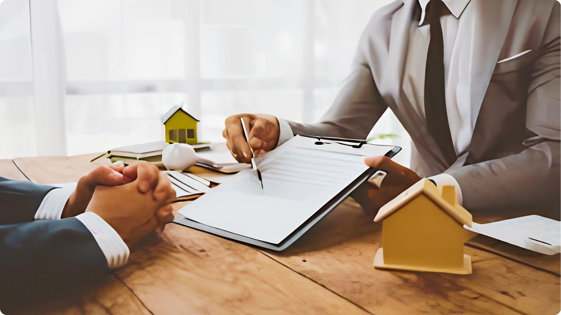 Business people finalize paperwork at a desk with house models present.