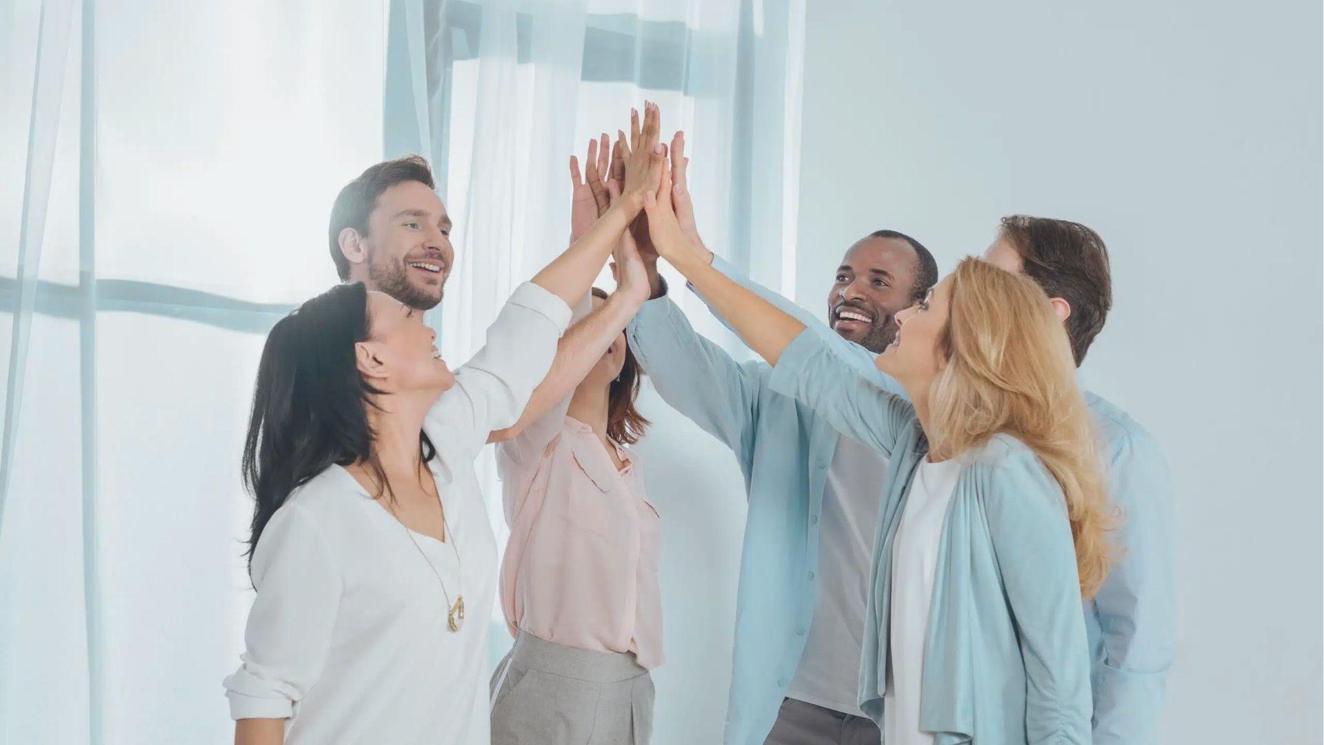 Six diverse colleagues in business casual attire high-five in a bright office.