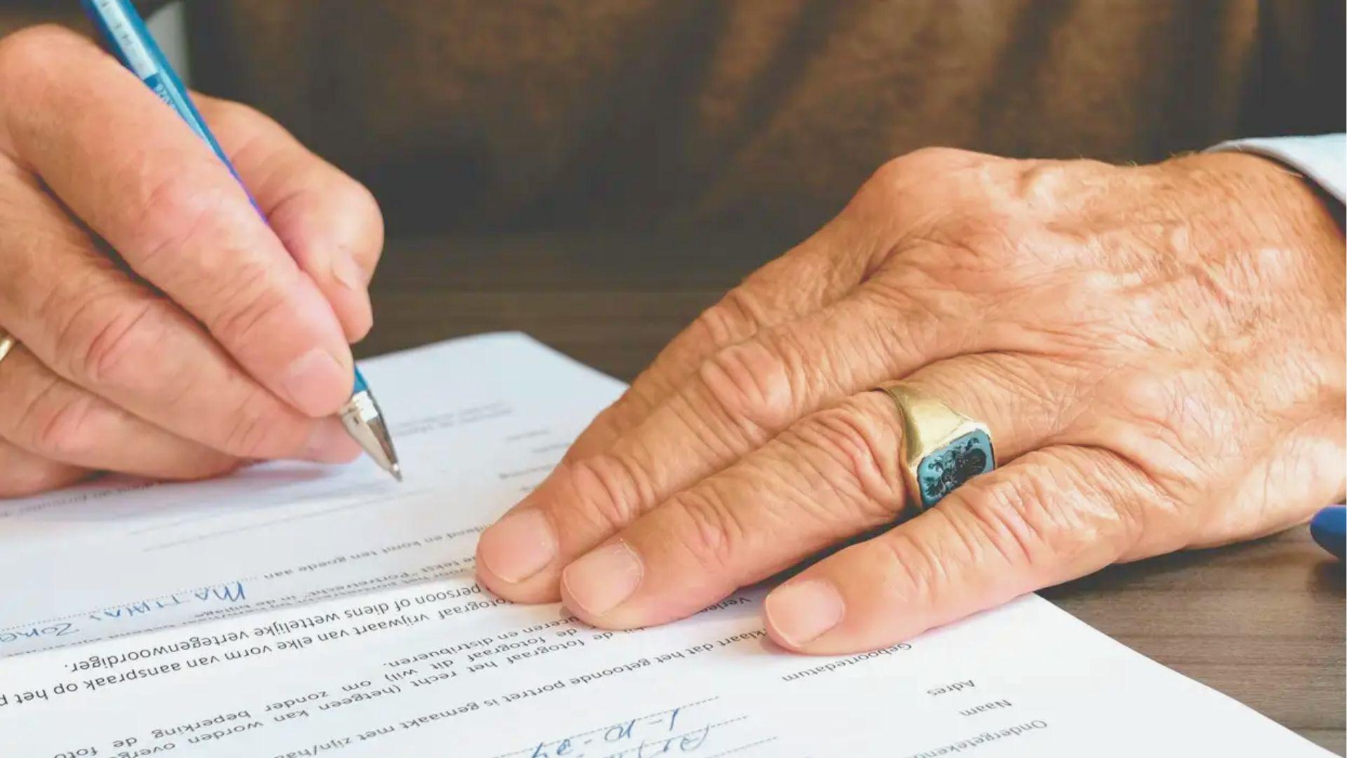 Close-up of an elderly person's hands signing a legal document with a pen.
