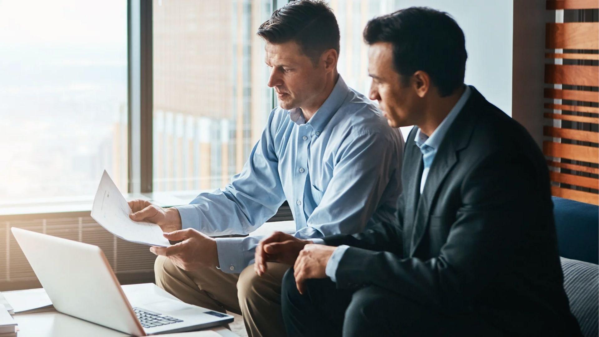 Two businessmen reviewing estate documents on a laptop in the office for Per Stirpes distribution.