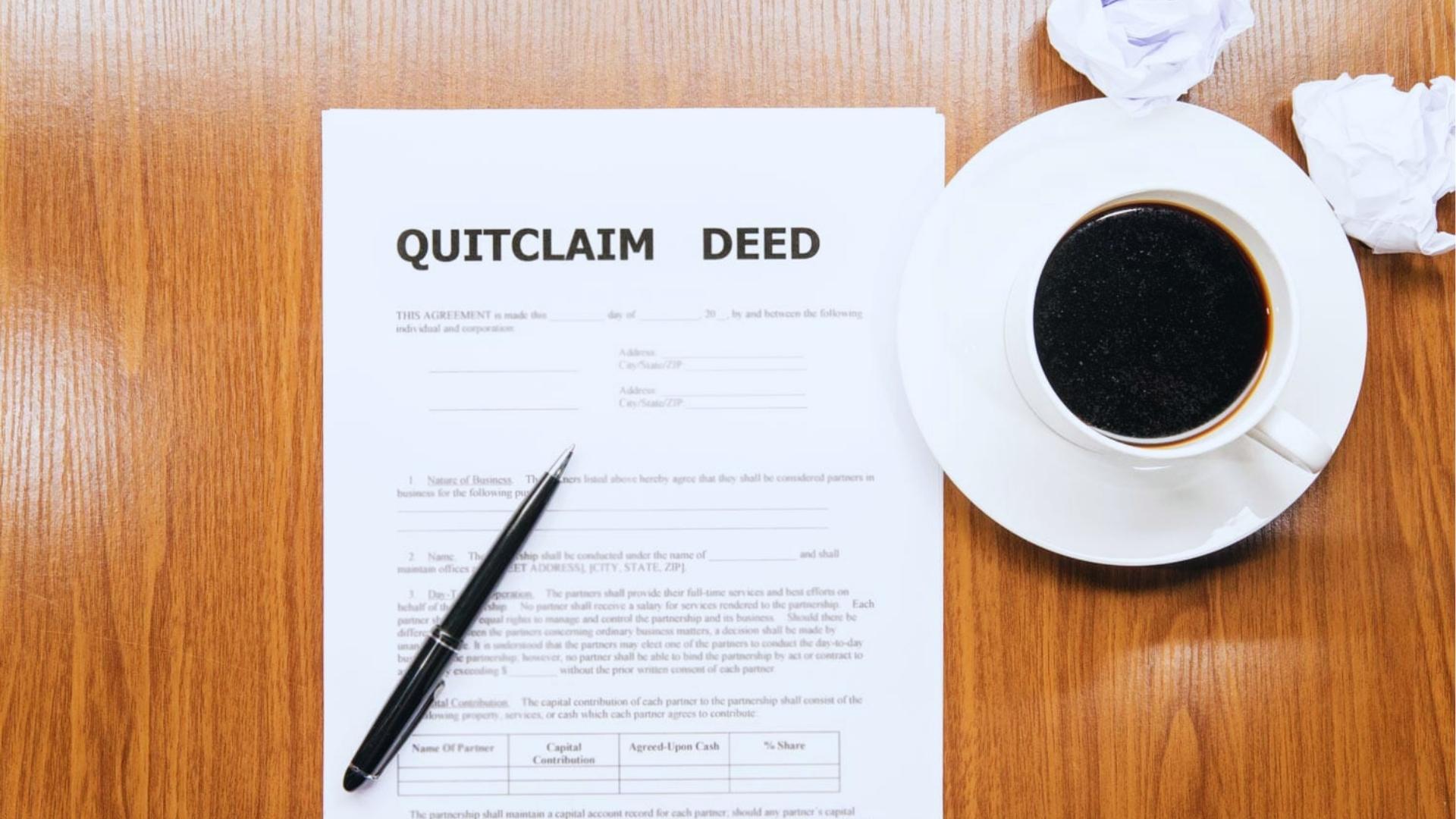 Quitclaim deed form lies on wooden desk beside black coffee, crumpled papers, and uncapped pen, showing document review process.