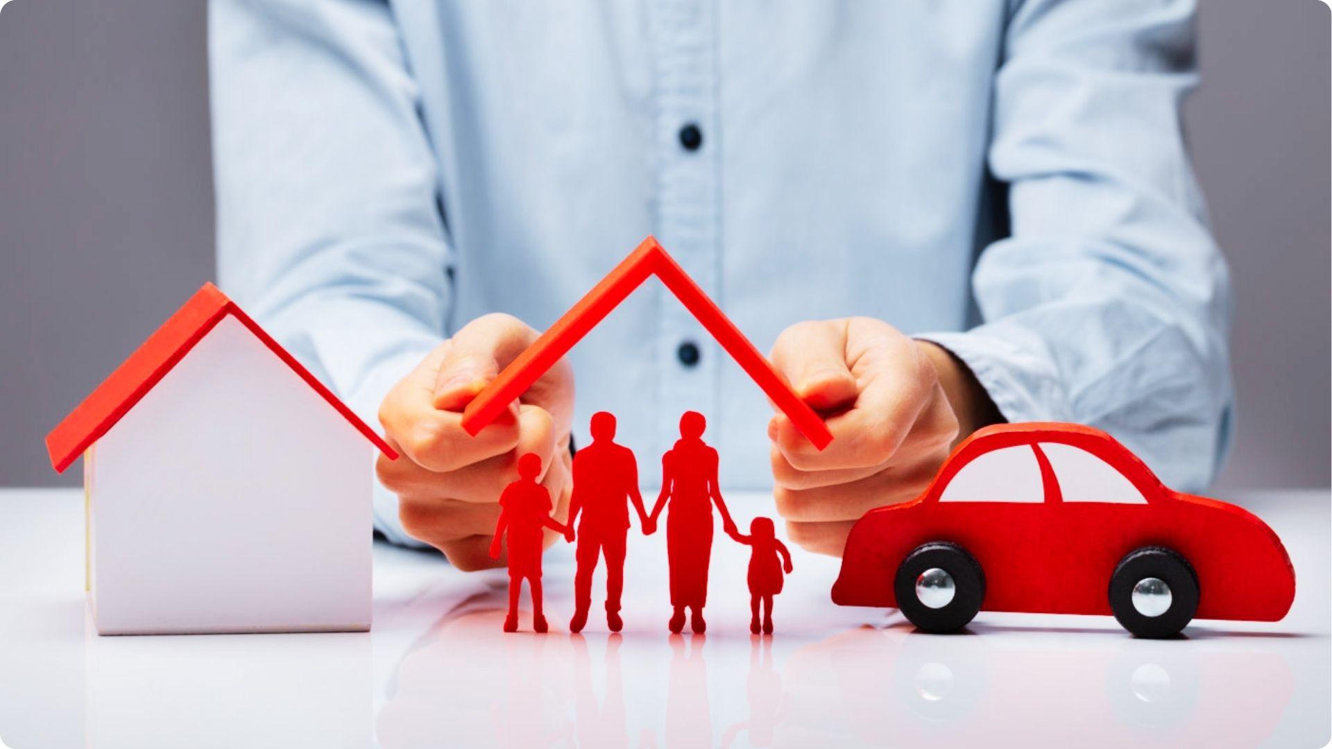 A person holds a red roof shape over red cutouts of a family, with a house and car model nearby.