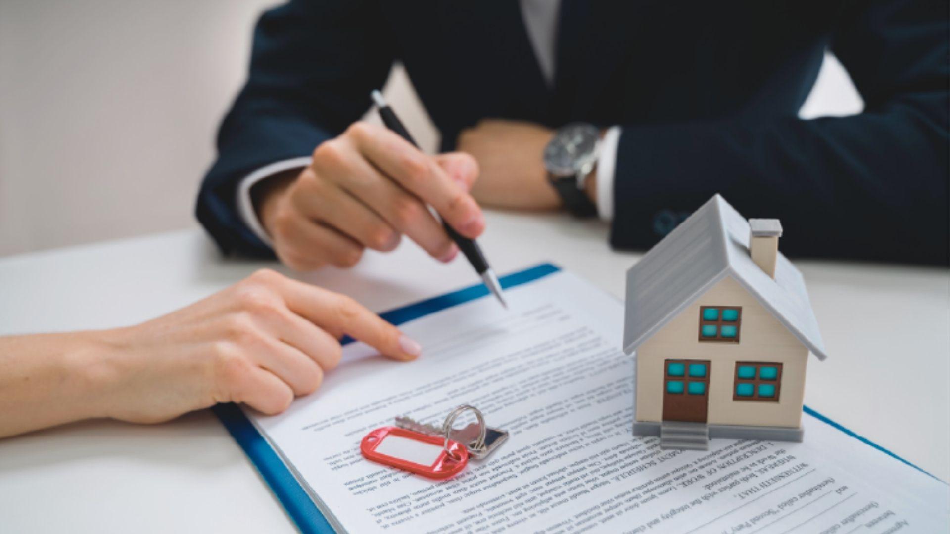 Real estate agent and client reviewing paperwork with a house model and keys placed on the signed contract.
