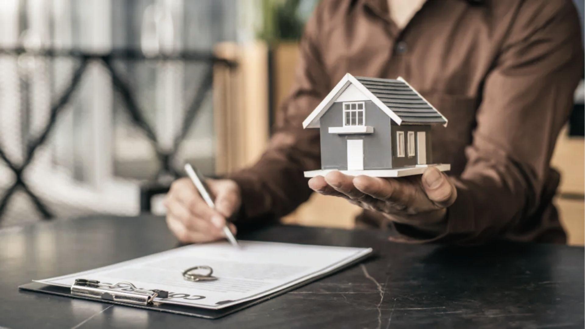Person holds model house while signing documents, showing Virginia adverse possession claims process.